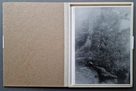 An open art portfolio box showing the paperback artist book cabbage white by Raymond meeks. the book has a forest landscape on the cover in black and white