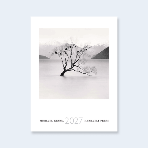 A minimalist calendar cover featuring a black and white photograph of a lone tree in a calm lake with mountains in the background, titled '2027' by Michael Kenna, published by Nazraeli Press.