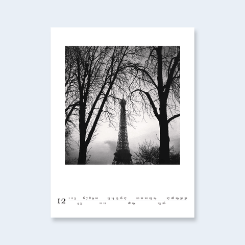 A minimalist calendar page featuring a photograph of the Eiffel Tower framed by bare winter trees.