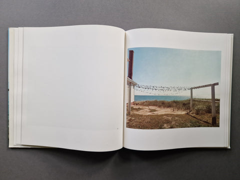 An open book, showing a mostly blank left page and a printed landscape photograph on the right page with a beach, dunes, and sky.