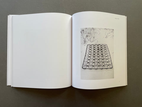 An open white art book or magazine laid flat on a dark gray surface, showing a black-and-white printed sketch or photograph of a geometric wire mat on the right page.