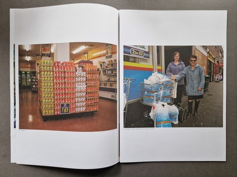 An open publication spread photographed from above on a dark surface. The left page shows a grocery store aisle with a large stacked display of bottled drinks.