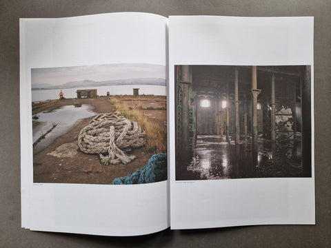 An open publication spread showing two printed photographs side by side on white pages, photographed from above on a dark gray surface.