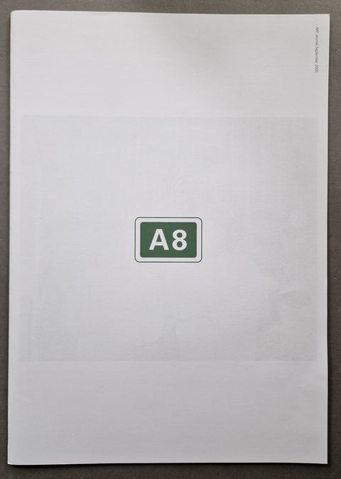 A white A8 paper newspaper publication cover centered on a dark gray surface, with a green and white 'A8' sign in the middle.