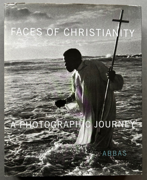 Book titled 'Faces of Christianity: A Photographic Journey' by Abbas with a cover featuring the image of a man holding a cross and walking into the ocean.