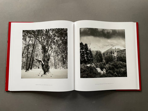 An open hardcover book with red edges, displaying two black and white landscape photographs on white pages against a dark gray background.