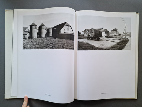 An open book showing two black-and-white photographic prints on the pages, photographed against a dark gray background.
