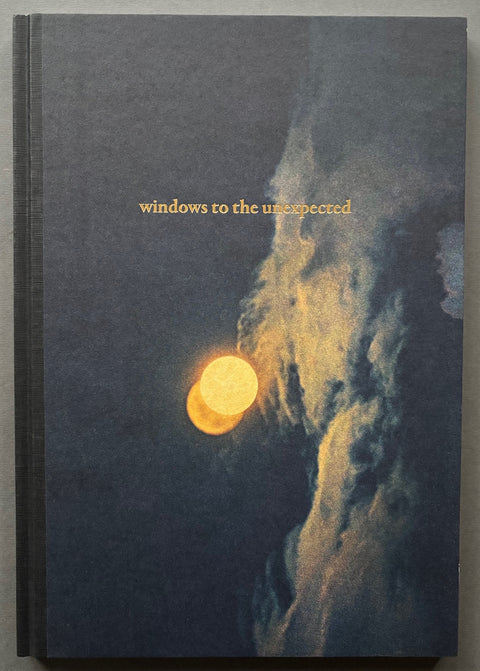 Book titled 'Windows to the Unexpected' by Albarran Cabrera' with a cover featuring the image of the sun above clouds.