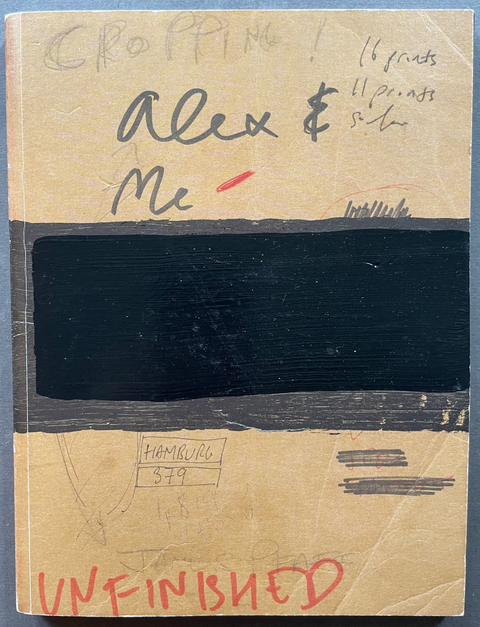 A beige front cover of Alex&Me by James Pfaff with a large black rectangular block, handwritten notes, and red 'UNFINISHED' text at the bottom, photographed flat on a blue-gray surface.