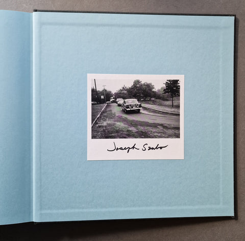 An open book showing a centered printed photograph of a vintage car on a road, with the signature 'Joseph Szabo'