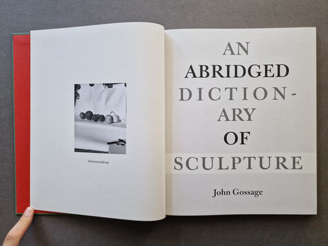 An open book titled 'An Abridged Dictionary of Sculpture' by John Gossage. The left page is white with a small black-and-white photograph, and the right page features large black text.