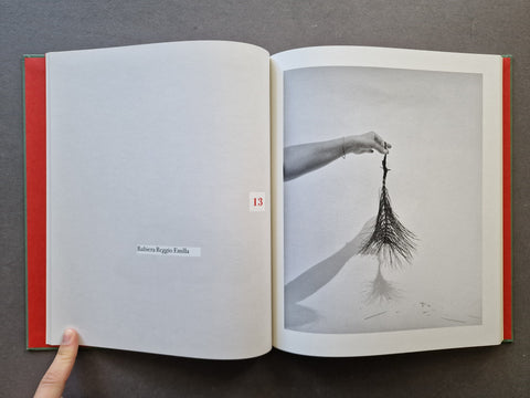 An open book showing a black-and-white photograph of a hand holding a bundle of roots on the right page.