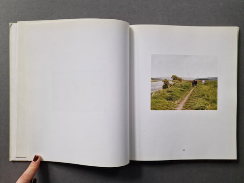 An open book, showing mostly blank white pages on the left and a printed landscape photograph on the right depicting a grassy path beside water.