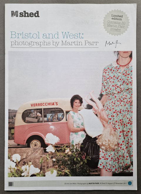 A flat lay photograph of a M shed magazine cover featuring Martin Parr's 'Bristol and West: photographs by Martin Parr' collection, with a vintage pink and cream bus, women in floral dresses, and white flowers.