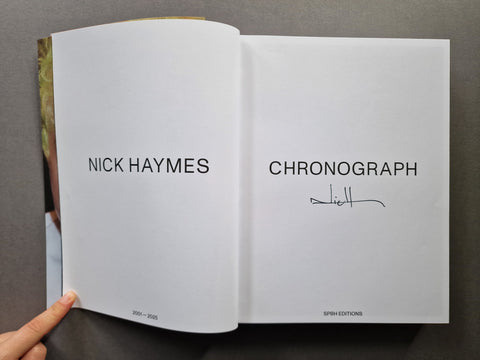 An open book, showing two white pages with the text 'NICK HAYMES' and 'CHRONOGRAPH,' plus a handwritten signature.