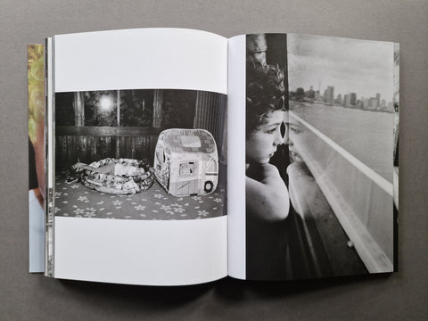 An open book, showing two printed pages with black-and-white photographs. The left page contains a photo of a kid in an inflatable pool and the right page shows a black-and-white portrait of a kid looking out a window beside a city skyline.