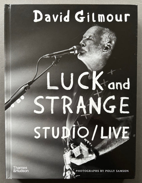 Book titled 'David Gilmour: Luck and Strange - Studio/Live' by Polly Samson with a black cover featuring the image of David Gilmour playing a guitar and singing into a microphone.