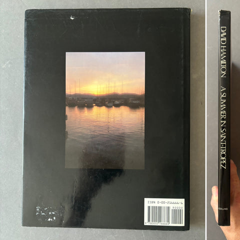 A hardcover book titled 'A Summer's Night' by David Hamilton and Sandra Perez, shown from the back with a scenic sunset photo in the center. A hand is holding the spine on the right to show thickness.