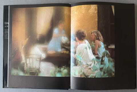 An open book or magazine spread showing two printed photographs side by side. The left page has a dark border and a softly lit, painterly scene with a seated figure in a blue dress.