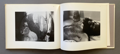 An open hardcover art book displayed flat on a dark gray surface, showing two black-and-white photographic prints on cream-colored pages.