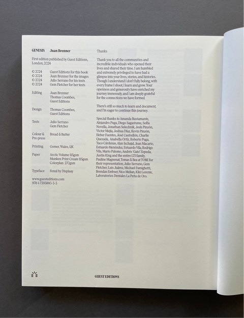 The back cover of a book on a dark gray surface, showing publication details, credits, and a list of contributors. The book is open, with the right page blank and the left page displaying the printed text.