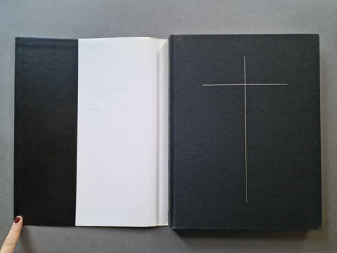 An open black book. The left page is white, and the right cover is black with a thin white cross design.