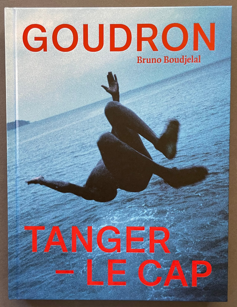 A book titled 'Goudron Tanger - Le Cap' by Bruno Boudjéal, featuring a cover photo of a diver in the ocean with bold red text, displayed on a brown surface.