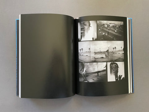An open hardcover book or photo journal laid flat on a neutral gray surface. The left page is blank with a dark gray tint, while the right page contains a collage of black-and-white photographs showing a street scene, a face, palm trees, and figures.