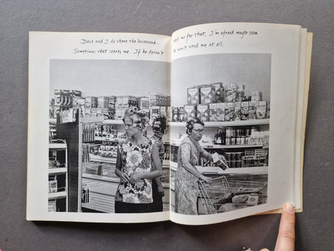 An open book. The pages show a black-and-white photograph of people in a grocery store aisle with handwritten text at the top of the left page.