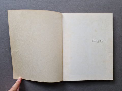 An open vintage book with blank, aged pages. The right page has a small handwritten title reading 'Growing up female'.
