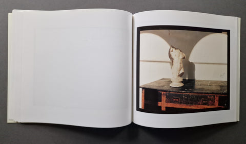 An open art book, showing a printed photograph on the right page of a white sculptural bust displayed on a dark table against a light background.