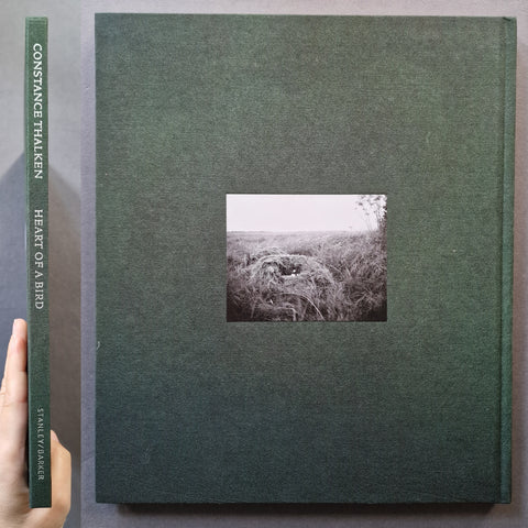 A hardcover book or album cover in dark green with a small black-and-white landscape photograph centered on the front. A hand is visible holding the spine on the left, and the title text reads Constance Thalken, Heart of a Bird