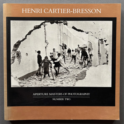 Book titled' Henri Cartier-Bresson: Aperture Masters of Photography' with a bronze cover featuring a black and white image of children playing in a ruined building.