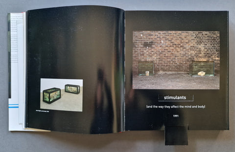 An open black art book, showing two interior pages with printed text and small photographs. The right page contains a brick wall photo and the title 'stimulants' with subtitle text below.