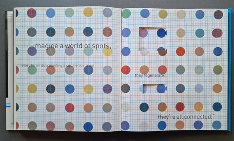 An open book showing two pages covered in a colorful pattern of paper circles on white graph paper, with printed text and a small cutout window on the right page.