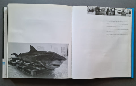 An open book showing a black-and-white photograph of a large shark on a platform on the left page, with small black-and-white inset photos and text on the right page.