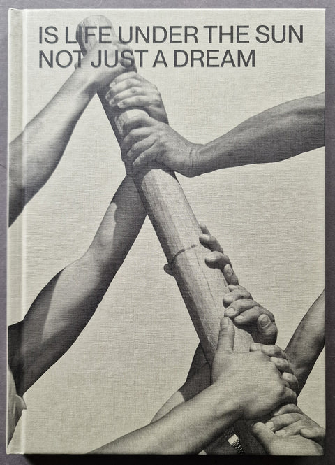 A square book cover featuring a black-and-white photograph of multiple arms gripping a wooden pole together, with the text 'IS LIFE UNDER THE SUN NOT JUST A DREAM' at the top.