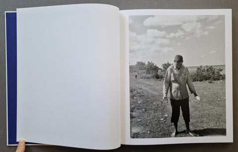 An open book with one blank white page on the left and a black-and-white printed photograph on the right showing a person standing outdoors.