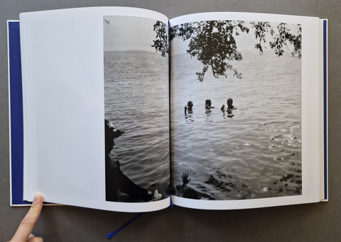 An open hardcover book, showing a black-and-white photographic print of people in the water across both pages.