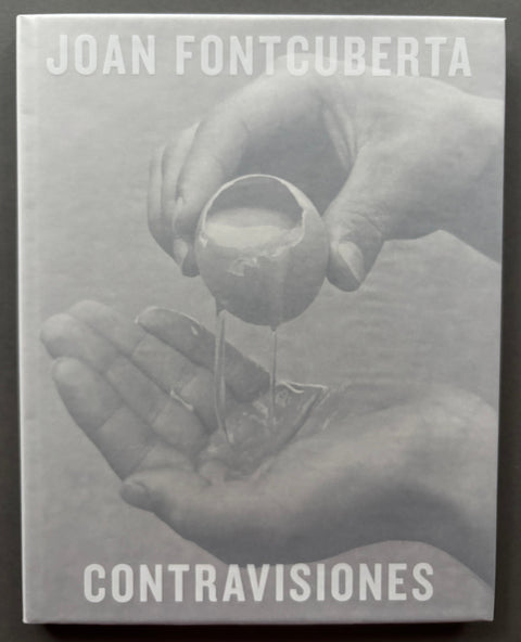 Book titled 'Contravisiones 1974-1989' by Joan Fontcuberta with a grey cover featuring the image of hands holding a cracked raw egg.