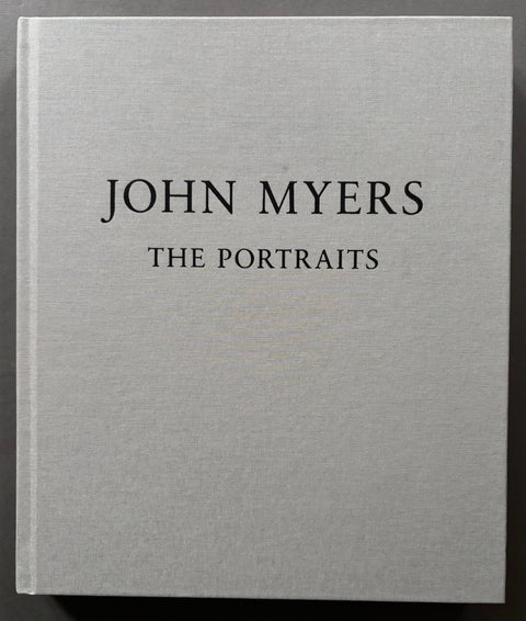 The front cover of the book 'John Myers: The Portraits' featuring a textured light gray linen cover with black serif text, photographed against a dark background.