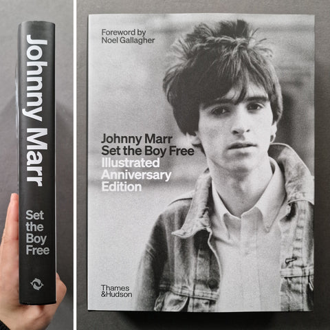 A book titled "Johnny Marr Set the Boy Free: Illustrated Anniversary Edition" shown standing upright with its black spine on the left, and the front cover on the right. A hand is holding the spine.