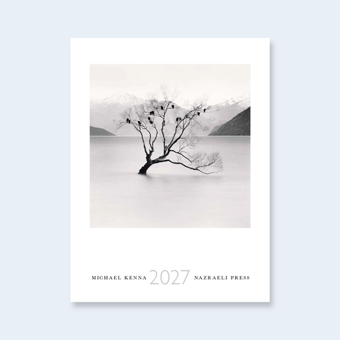 A minimalist calendar cover featuring a black and white photograph of a lone tree in a calm lake with mountains in the background, titled '2027' by Michael Kenna, published by Nazraeli Press.