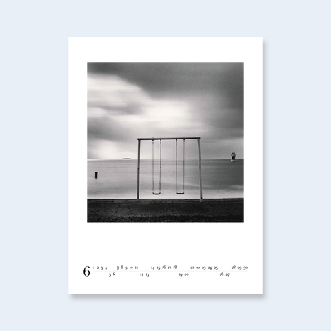 A minimalist calendar print featuring a photograph of a swing set by the sea.