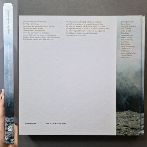 A square book cover photographed from above on a dark surface. The main cover is white with black text and a small grayscale landscape photo in the lower right corner.
