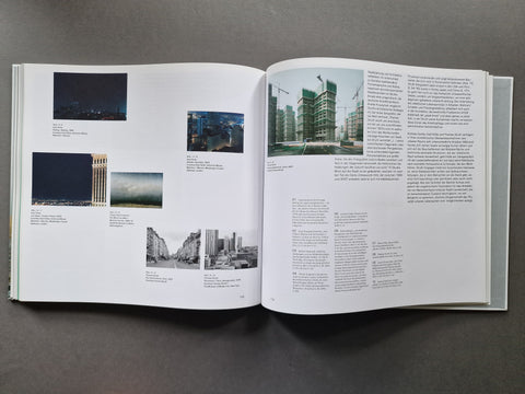An open book spread on a dark gray surface, showing printed text columns and several architectural photographs on white pages.