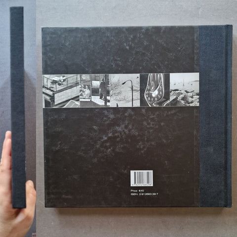 A hardcover book shown from the back, with a hand holding the matching dark blue spine on the left.