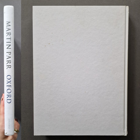 A white hardcover book shown upright against a dark gray background, with its front cover blank and the spine visible on the left. The spine reads 'MARTIN PARR OXFORD' in blue text.
