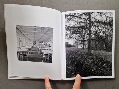 An open book showing two black-and-white photographic prints: an interior dining or exhibition space on the left page and a tree-lined outdoor scene on the right page.