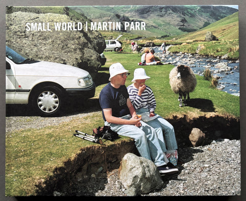 Book titled 'Small World' by Martin Parr with a cover featuring an image of people sitting by the side of a river being looked at by a sheep.